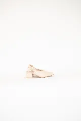 Zapato de tacón medio y punta fina en charol color off-white, con diseño destalonado y tira ajustable con hebilla dorada en el talón.