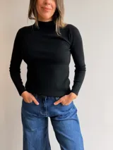 Media polera de tejido fino color gris, con cuello alto, manga larga y corte ajustado al cuerpo.