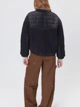 Campera crop de corte boxy y color negro, forrada en corderito, con parches capitoneados en el pecho y las mangas. Cuenta con cierre frontal metálico, cuello alto, puños y bajo elastizados, y detalle de logo bordado en hilo en el pecho.