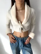 Top de manga larga color negro, con cuello y puños de piel sintética. Presenta un cierre frontal con lazo ajustable.