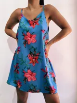 Vestido corto celeste con estampado de flores rojas y hojas verdes, de breteles finos y corte suelto.