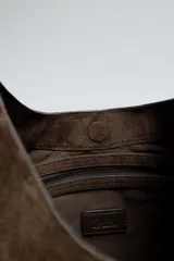 Bolso de hombro marrón con efecto serraje. Tiene un compartimento principal con cierre magnético y un bolsillo interior con cremallera. El asa es del mismo material.