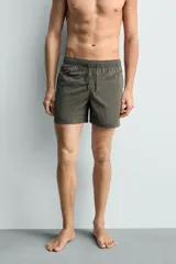 Bañador de hombre de largo medio, color celeste claro con rayas blancas horizontales. Presenta cintura elástica ajustable con cordón, bolsillos frontales y bolsillos traseros de plastrón. Incluye forro interior.