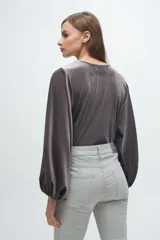 Blusa de terciopelo gris con acabado brillante, cuello redondo y mangas largas abullonadas con puños elásticos.