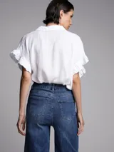 Camisa blanca de lino con cuello clásico, mangas cortas con volados y cierre frontal con botones.