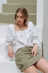 Blusa blanca con bordado inglés, escote cuadrado, mangas largas abullonadas con volados y cierre frontal con botones.