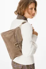 Bolso de hombro color chocolate, confeccionado en gamuza, con diseño de solapa frontal y detalle de herraje metálico dorado en forma de estribo. Incluye correa ajustable con ganchos metálicos.