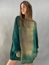 Buzo tejido de lana merino con diseño oversize, manga ranglan y cuello levemente elevado. Presenta un efecto de teñido degradado que combina tonos verdes y beige.