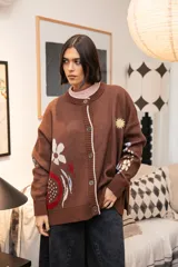Saco tejido color chocolate con diseño inspirado en la granada, con flores y soles bordados. Presenta cierre frontal con botones, cuello redondo y puños acanalados.