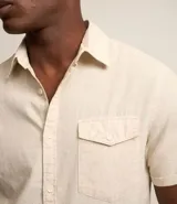 Camisa de hombre de manga corta color marrón, confeccionada en lino y algodón. Presenta cuello clásico, botonadura frontal, bolsillo en el pecho y mangas con botón para enrollar.