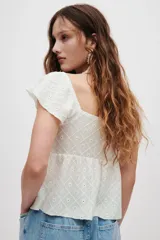 Blusa corta blanca en punto pointelle con textura, escote corazón, mangas cortas circulares, detalle cut-out con cordón de ajuste en el busto y diseño acampanado con costura fruncida.