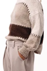 Sweater de tejido de punto grueso con diseño de bloques de color en tonos beige, marrón y bordó. Presenta un corte relajado, mangas amplias y detalles de costuras visibles en contraste que separan las franjas de color.