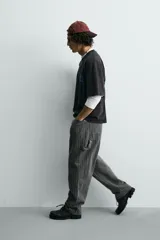 Pantalón de corte ancho (baggy fit) color verde oscuro/gris oscuro con finas rayas verticales blancas. Presenta cintura ajustable con trabillas laterales, bolsillos delanteros, bolsillos traseros de plastrón, bolsillo cerillero y una tira multifunción en la pernera.