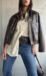 Camisa de color beige con diseño de broderie anglaise, cuello clásico, cierre frontal con botones y mangas largas.