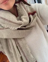 Bufanda de gran tamaño en color beige con diseño de cuadros sutiles en tono bordó y bordes deshilachados.
