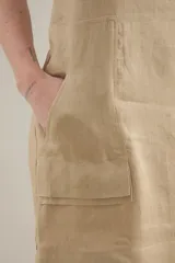 Vestido midi de lino color beige, de silueta relajada, escote redondo, sisas amplias y bolsillos delanteros aplicados.
