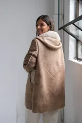 Tapado tipo gamuza con interior de corderito sintético, color beige con detalles en crudo. Presenta capucha, cierre frontal completo y puños con vuelta de corderito.