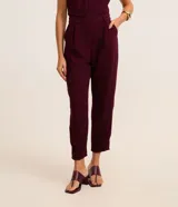 Pantalón zanahoria color borgoña de crepé de poliéster, con trabillas en la cintura, cierre tradicional, pliegues y bolsillos.