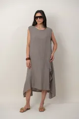Vestido midi de lino color beige, sin mangas y con cuello redondo. Cuenta con un diseño irregular con detalle de volado vertical a un costado.