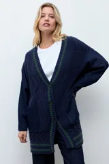 Sacón de punto con frente y espalda en tejido de ochos color azul marino, con detalles de rayas verdes en el borde. Las mangas son de tela de jean azul oscuro. Presenta cierre frontal con botones y bolsillos laterales.