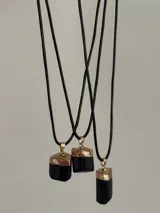 Collar con cordón de cuero negro y dije rectangular de piedra negra con detalles dorados.