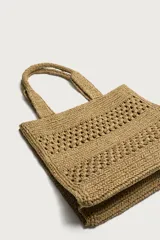 Bolso tipo shopper de color naranja con acabado trenzado y diseño estructurado. Cuenta con compartimento principal y dos asas cortas de mano.