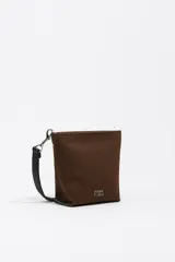 Bolso bandolera de gabardina color marrón, con diseño compacto, cierre de cremallera y asa de tejido ajustable. Presenta el logo de la marca aplicado en la parte frontal.