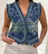 Chaleco corto en denim azul con detalle desflecado y bordado artesanal en tonos celeste y dorado. Estilo boho chic con escote en V, ideal para combinar con prendas básicas y elevar tu look.