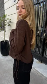 Buzo de punto color chocolate con textura acanalada, cuello redondo y diseño ajustable en los laterales mediante tiras que permiten regular el largo.