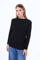Buzo de tejido de punto fino en color negro, con cuello redondo y mangas largas. Presenta detalles de terminación con borde ondulado en color blanco en el cuello y en los puños.