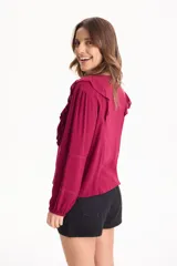 Blusa de viscosa color blanco con escote en V y cordón ajustable, mangas largas y volados decorativos en los hombros.