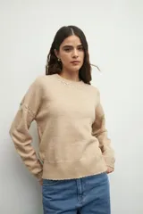 Sweater de tejido de punto color marrón, con cuello redondo y detalles de calados decorativos en el cuello y las mangas. Presenta un diseño de corte recto y manga larga.