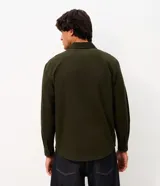 Camisa de manga larga confeccionada en sarga de algodón color verde militar. Presenta cuello inglés, cierre frontal con botones y dos bolsillos con solapa en el pecho.