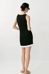 Vestido corto de punto canalé negro, con cuello barco, sin mangas y detalle de volados blancos en el borde inferior.