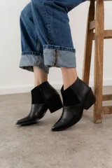 Botín de cuero negro con paneles laterales de gamuza y cierre de cremallera en el lateral interior. Tiene puntera fina y tacón bloque de altura media.