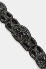 Cinturón elástico negro con diseño ornamental bordado de cuentas de vidrio facetadas y detalles metálicos en tono plateado.