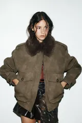 Cazadora color verde militar con efecto ante, cuello solapa con aplicación de pelo sintético desmontable, manga larga con puño, trabillas en los hombros y bolsillos frontales con solapa y botón. Cierre frontal con cremallera y botones ocultos.