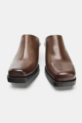 Zueco tipo mule de piel marrón con efecto desgastado, punta cuadrada y tacón bajo en bloque negro.