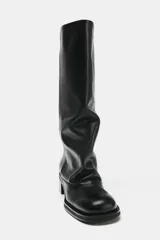 Bota alta de piel estilo biker, color negro, con diseño slouchy y puntera semi cuadrada. Cuenta con tacón bajo y ancho.