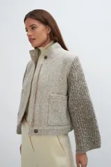 Campera de lana fina color crema, con cuerpo estructurado y mangas de tejido de punto acanalado. Presenta cuello alto, cierre frontal con botones y bolsillos laterales con doble abertura.