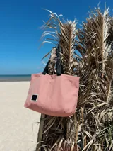 Bolso tipo tote rayado en tonos rosa y blanco, con asas cortas negras y correa larga regulable negra.