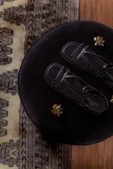 Sandalias planas de cuero negro con múltiples tiras finas adornadas con tachas doradas. Cuentan con cierre de hebilla en el tobillo.