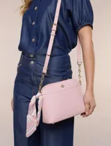 Cartera bandolera estructurada de eco cuero rosado con textura graneada, silueta curva y cierre superior. Posee correa larga regulable con detalles de cadena dorada, bolsillo frontal con logo metálico, pañuelo estampado a contratono anudado en un lateral y base rígida con apoyos metálicos.