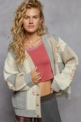 Cardigan de punto con diseño patchwork en bloques de color gris, blanco y beige, de manga larga abullonada, cuello en V y cierre frontal con botones.