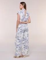 Enterito largo color blanco con estampa ilustrada en azul estilo Toile de Jouy, escote en V cruzado, mangas cortas caídas, bolsillos laterales, pantalón amplio wide leg y cinturón incorporado con hebilla metálica.