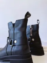 Bota corta negra de cuero, con caña media, hebilla lateral y suela track.