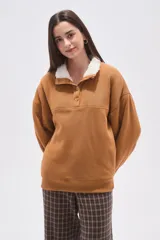 Buzo de algodón color tostado, con cuello polo y cierre frontal parcial con botones. Presenta un detalle de forro de corderito sintético blanco en el cuello y mangas largas con diseño holgado.