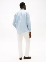 Camisa de hombre Tommy Hilfiger de algodón Oxford elástico, color celeste con rayas verticales finas en blanco y rojo. Tiene corte regular, cuello abotonado, bolsillo de parche en el pecho y logo bordado en el bolsillo.