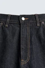Jeans de denim oscuro, corte ancho (baggy fit) y tiro medio, con costura central girada en el frente de ambas piernas. Presenta pespuntes en color caramelo.