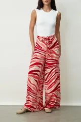 Pantalón ancho de tiro alto, color rojo y rosado, con estampado abstracto tipo cebra o remolino. Presenta un lazo para atar a la cintura.